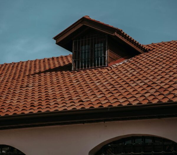A traditional red tiled roof with an attic window under a clear blue sky, showcasing classic architecture.