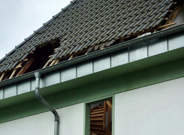 An exterior view of a damaged house showing a broken roof and exposed interior structure.