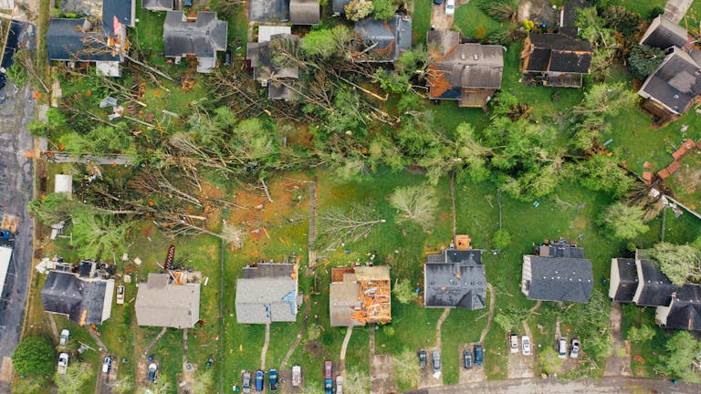 Drone dramatic view of small settlement cottages with ruined roofs and windthrown trees after massive storm